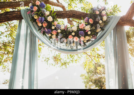 Sunset wedding ceremony, arch decorated with grey cloth hanging on big tree and rose flowers arrangement Stock Photo