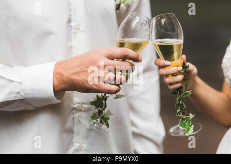 Man and woman hands holding two champagne glasses decorated with flowers for wedding ceremony Stock Photo