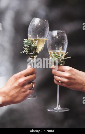 Man and woman hands holding two champagne glasses decorated with flowers for wedding ceremony Stock Photo