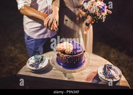 Wedding couple cutting beautiful purple cake decorated with rose flowers and fresh berries Stock Photo