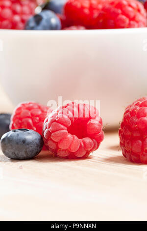 lying on a light board of raspberries and blueberries during the harvest, in the background a white plate full of berries Stock Photo