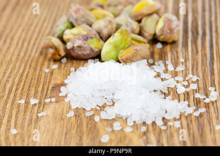 a bunch of peeled pistachios and large sea salt lying on an old wooden table, focus on salt crystals, close-up Stock Photo
