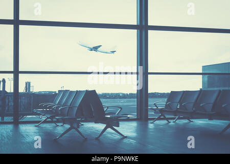 Traveling concept - empty interior of the airport lounge on the background of flying aircraft (blue filter effect) Stock Photo