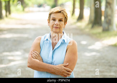Emotion, age and people concept - portrait of a beautiful senior woman in the park looking serious and thoughtful at the camera Stock Photo