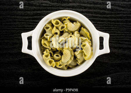 Pasta creste di gallo in a ceramic pot flatlay spinach raw isolated on black wood background top view Stock Photo