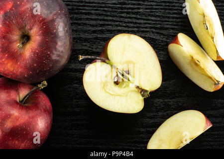 Sliced red delicious apples flatlay on black wood background two whole one half and three slices Stock Photo