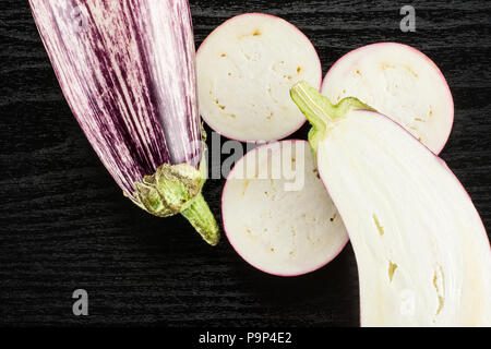 Striped purple eggplants set top view isolated on black wood background whole one half and sliced three rings Stock Photo