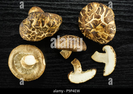 Group of four whole two slices of fresh raw brown shiitake mushroom flatlay isolated on black wood Stock Photo
