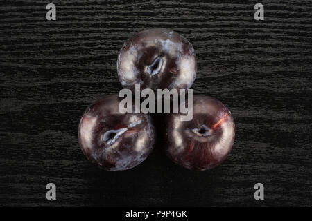 Three red blue plums table top isolated on black wood background round whole fresh juicy fruit Stock Photo