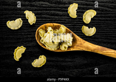 Pasta creste di gallo in a wooden olive spoon flatlay isolated on black wood background top view spinach raw Stock Photo