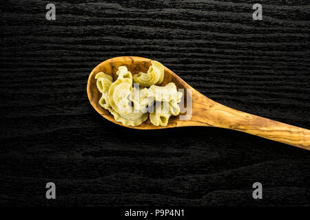 Pasta creste di gallo in a wooden olive spoon flatlay spinach raw isolated on black wood background top view Stock Photo