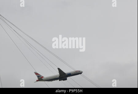 The Boeing 777-200 of British Airways pictured through electrical wires as it takes off from Heathrow airport, London, UK Stock Photo