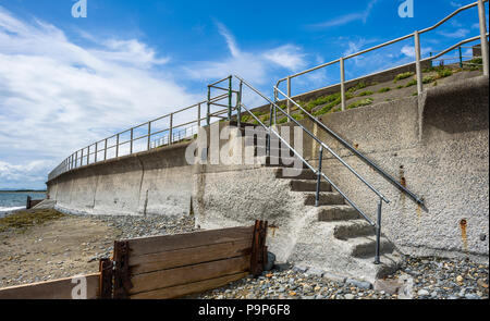 Sea wall, steps and wooden groynes and rusting metal to protect the sea coast at Criccieth beach, Wales UK. Stock Photo