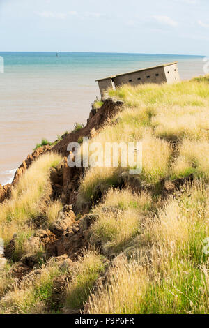 A Second world War lookout post leaning alarmingly and about to tumble over the edge of the cliff near Aldbrough on Yorkshires East Coast, UK. The coast is composed of soft boulder clays, very vulnerable to coastal erosion. This section of coast has been eroding since Roman times, with many villages having disappeared into the sea, and is the fastest eroding coast in Europe. Climate change is speeding up the erosion, with sea level rise, increased stormy weather and increased heavy rainfall events, all playing their part. Stock Photo