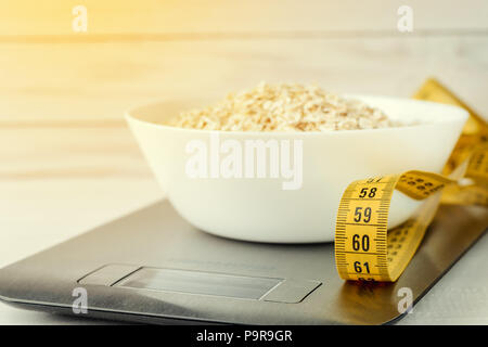 Diet concept, proper nutrition, healthy eating. Oatmeal in a white plate on the kitchen scale. Stock Photo