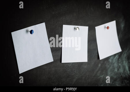 Three white stickers on black board pinned with colored studs Stock Photo