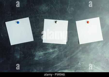 Three white stickers on dark board pinned with colored studs Stock Photo