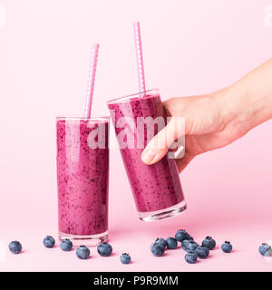 Two glasses of blueberries smoothie with straws on pink background. Woman's hand holding one glass. Healthy summer drink. Stock Photo