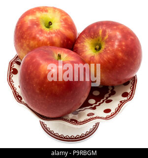 Three whole red Kanzi apples on plate isolated on white background Stock Photo
