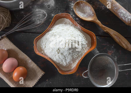 Old kitchen table with utensils and products for the test. Wheat flour in a ceramic dish and chicken eggs for the dough preparation. Rustic style. Top Stock Photo