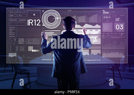Scanning new information. Attentive software developer using modern virtual reality glasses while being in his comfortable office and analyzing the in Stock Photo
