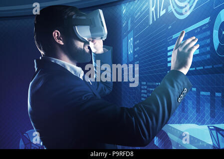 Using modern technologies. Positive enthusiastic programmer smiling and feeling satisfied with the result of his work while wearing virtual reality gl Stock Photo