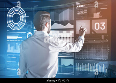 Touching transparent screen. Calm clever programmer carefully touching the transparent screen and feeling interested while working with a new device Stock Photo