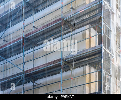 Scaffolding on the shell of a large new building, with a net to protect passers-by from falling objects, construction site Stock Photo