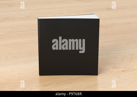 Blank black square soft cover book standing on wooden background. Isolated with clipping path around book Stock Photo