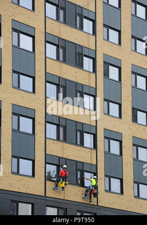 Two window cleaners use abseiling ropes to access windows on a new tower block in Portsmouth town centre, Hampshire, UK Stock Photo