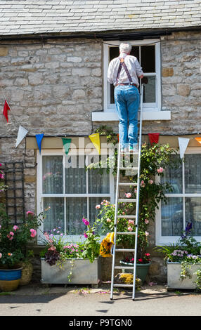Man up a ladder working on the window of a cottage, Tideswell, Derbyshire Stock Photo