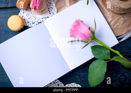 A bouquet of roses is pink, in gray paper and a white heart. Rose on an open notebook. Sweet pasta macaroons of different colors, on Valentine's Day. A free place for text or advertising Stock Photo