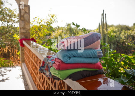 a pile of folded towels ready for a beach outing rest on a terrace wall with garden in sunlight in background Stock Photo