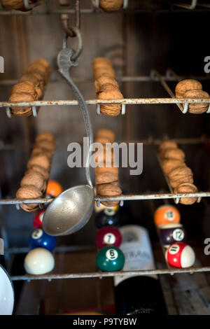 detail of unusual collection of objects displayed in old rack, including walnuts, pool balls, an old ladle and a bottle of wine Stock Photo
