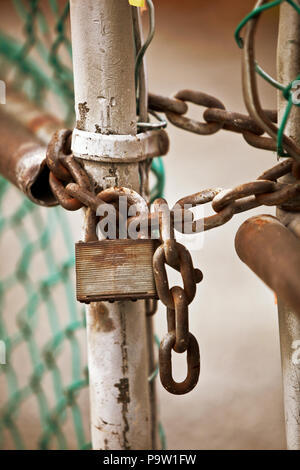 Rusty lock and chain securing a partially opened chain-link fence Stock Photo