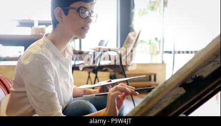 Young woman painter with color palette and paint brush in hand and ...