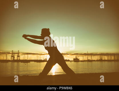 Woman practising Tai Chi and Yoga on city beach Stock Photo