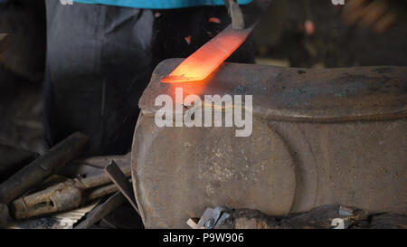 Blacksmith working metal with hammer on the anvil in the forge. hammer forging hot iron at anvil. Blacksmiths make machete. Hands of the smith by the work. Philippines. Stock Photo