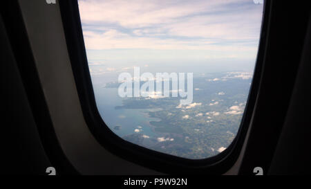 View through an airplane window on the tropical island, ocean, sky and clouds. Aerial view sea, clouds and sky as seen through window of an aircraft. Travel concept. Stock Photo