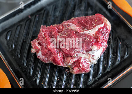 Close-up raw tasty fresh rib eye steak on grill cast iron pan. Organic beef meat seasoned with ground pepper cooked on barbecue. Stock Photo