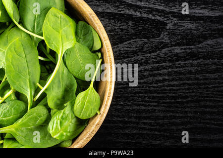 Fresh baby spinach leaves in a wooden bowl top view on black wood background Stock Photo