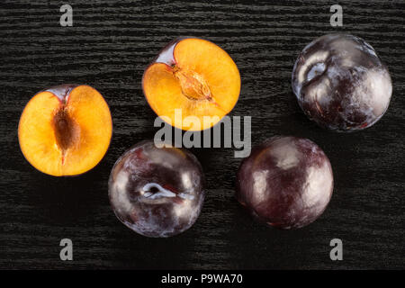 Red blue plums three whole two sliced halves table top isolated on black wood background Stock Photo