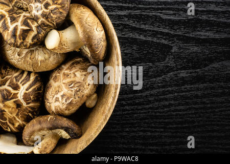 Fresh raw brown shiitake mushroom in a wooden bowl flatlay isolated on black wood Stock Photo