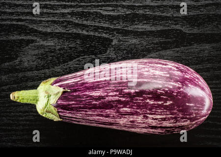 One striped purple eggplant top view isolated on black wood background Stock Photo
