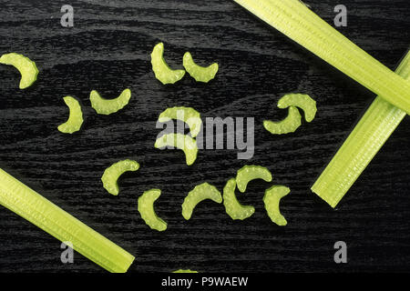 Three green celery sticks with fresh chopped pieces isolated on black wooden background Stock Photo