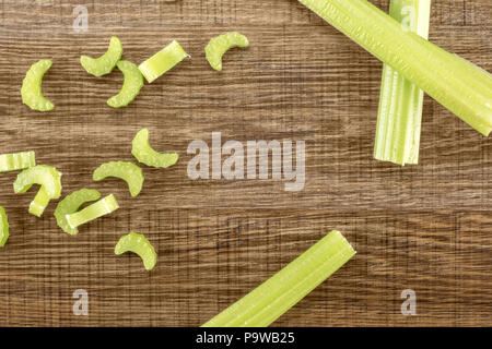 Three green celery sticks with fresh chopped pieces isolated on wooden background Stock Photo