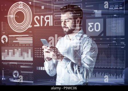 Reading messages. Cheerful young programmer looking glad and smiling while reading messages in his modern smartphone Stock Photo