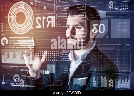 Careful touch. Calm serious web developer working with the information on the transparent screen and looking concentrated Stock Photo