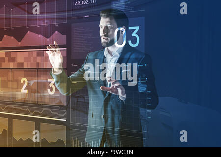 Worried man. Young emotional IT manager standing in front of a futuristic computer and feeling worried while looking at the information on the screen Stock Photo