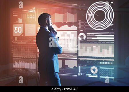 Thoughtful web developer. Professional software developer thoughtfully touching his beard and looking attentively at the information on the transparen Stock Photo